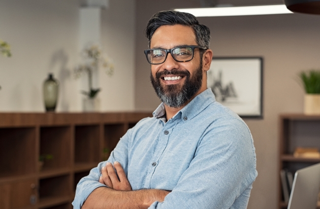 A businessman with glasses smiling in an office, highlighting the value of financial advisors for business owners and entrepreneurs.