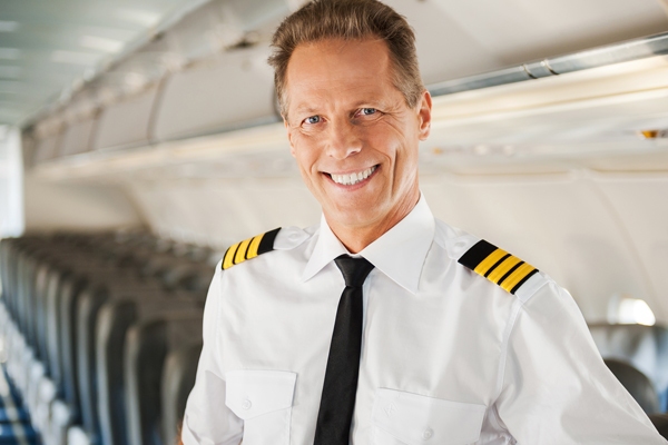 Smiling airline pilot standing in an aircraft aisle, representing specialized financial advisory services for pilots.