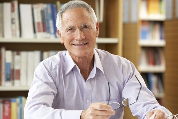 Smiling retired pilot seated in a library, holding glasses, representing a sense of accomplishment and readiness for retirement planning.