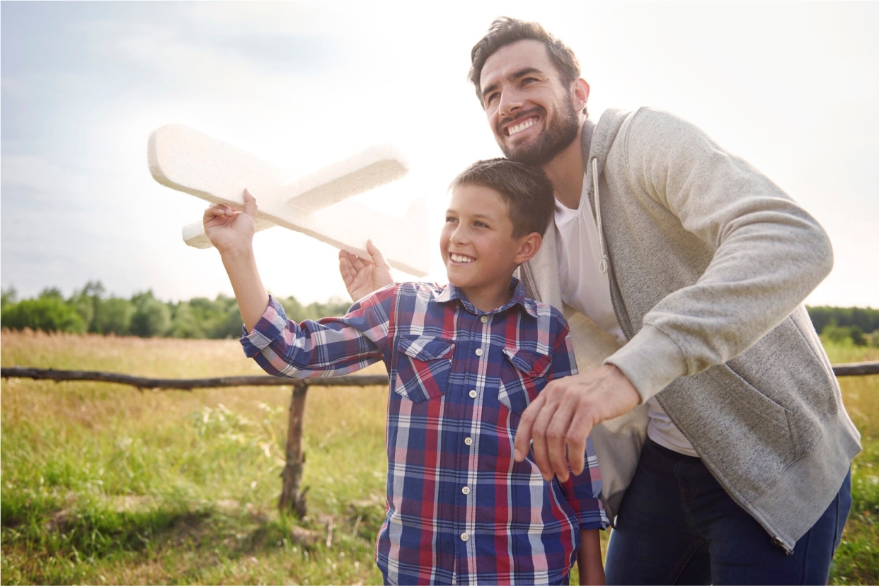 Photograph of a man with a boy outdoors holding a wooden airplane, symbolizing generational wealth planning for families.