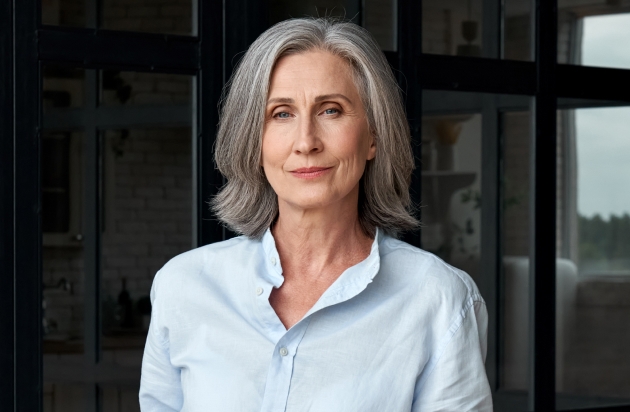 A confident elderly woman standing in a modern office, symbolizing the importance of wealth management and financial planning for corporate executives.