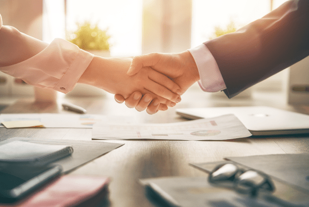 Two individuals shaking hands over a desk with documents, symbolizing collaboration in insurance services and financial planning insurance.