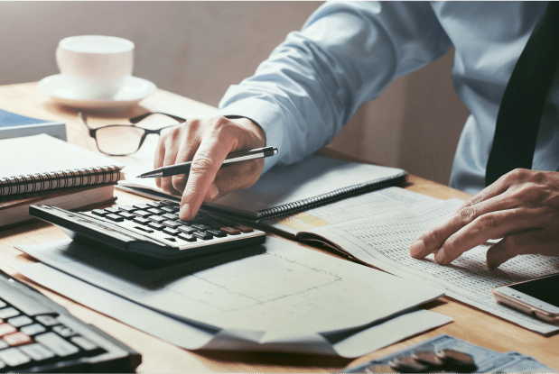 Man seated at a desk, using a calculator and holding a pen, representing tax planning services with support from tax planning advisors.