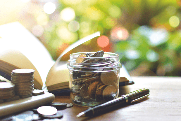 Jar of coins, open notebook, pen, and calculator on a desk, representing investment management services.